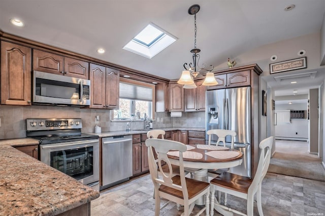 kitchen with pendant lighting, lofted ceiling with skylight, decorative backsplash, light stone countertops, and stainless steel appliances