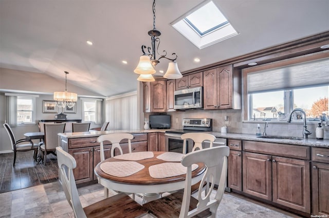 kitchen featuring lofted ceiling with skylight, sink, appliances with stainless steel finishes, decorative light fixtures, and a chandelier