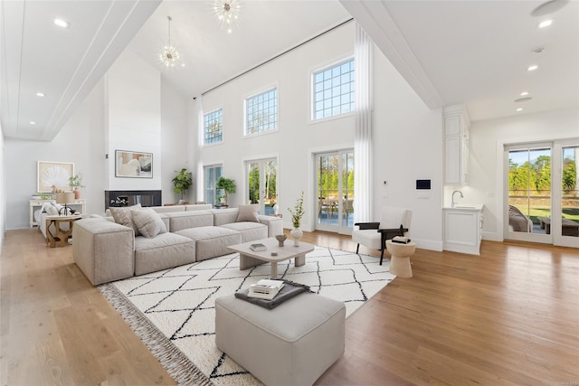 living room featuring sink, an inviting chandelier, a towering ceiling, and light wood-type flooring