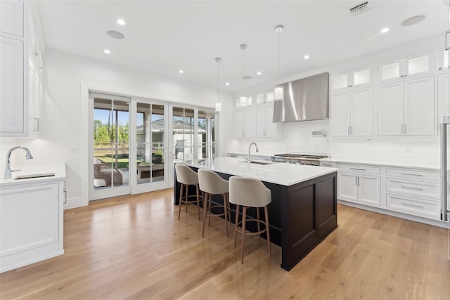 kitchen with white cabinetry, sink, a kitchen island with sink, and wall chimney range hood