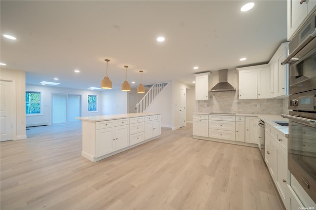 kitchen with white cabinetry, wall chimney range hood, tasteful backsplash, decorative light fixtures, and light wood-type flooring