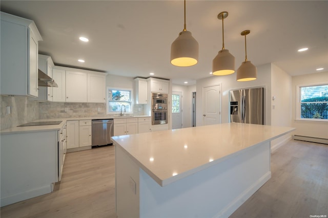 kitchen featuring sink, range hood, decorative light fixtures, a kitchen island, and appliances with stainless steel finishes