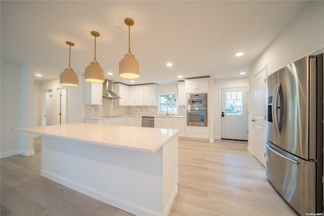 kitchen with backsplash, white cabinets, wall chimney range hood, appliances with stainless steel finishes, and decorative light fixtures