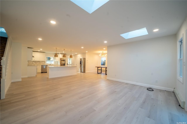 unfurnished living room with a skylight, baseboard heating, and light hardwood / wood-style floors