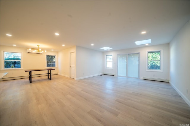 empty room featuring a chandelier, a skylight, baseboard heating, and light hardwood / wood-style flooring