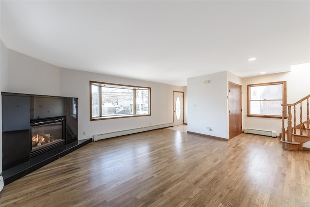 unfurnished living room with wood-type flooring, baseboard heating, and a healthy amount of sunlight