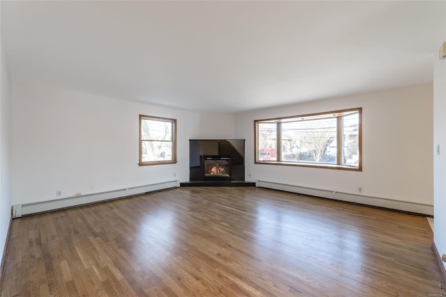 unfurnished living room featuring a baseboard radiator, a wealth of natural light, and hardwood / wood-style flooring