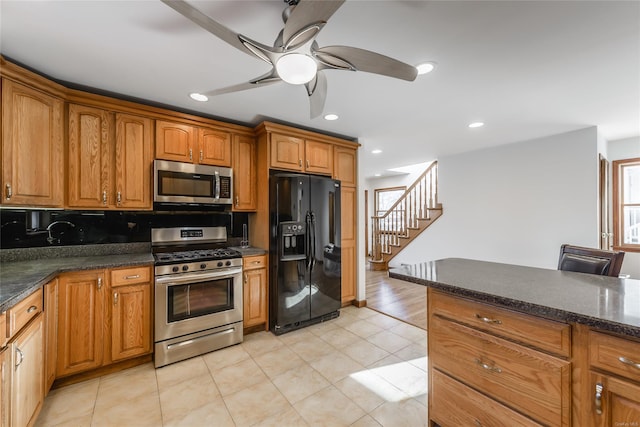 kitchen with appliances with stainless steel finishes, backsplash, dark stone counters, ceiling fan, and light tile patterned floors