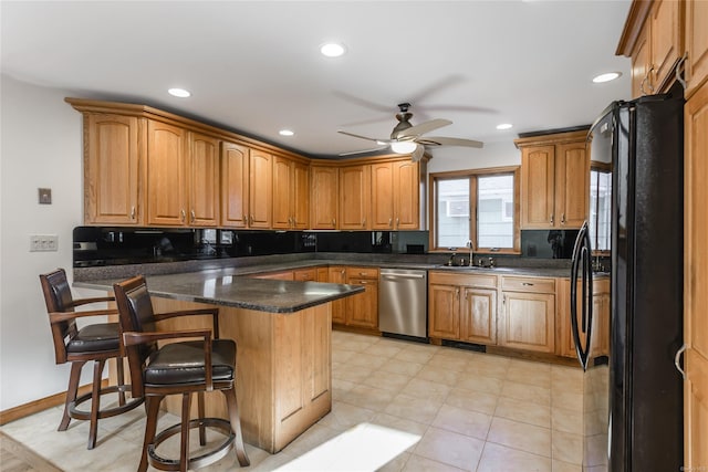 kitchen featuring black fridge, stainless steel dishwasher, a breakfast bar, ceiling fan, and sink