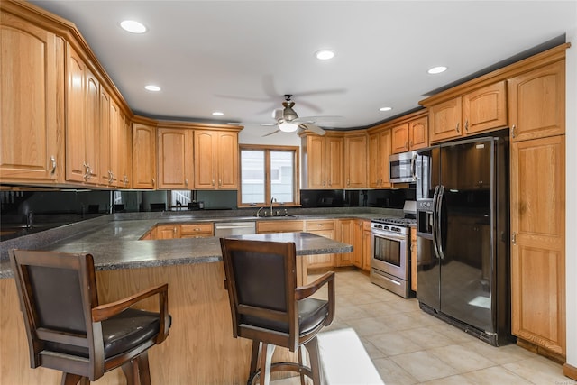 kitchen with a kitchen breakfast bar, sink, ceiling fan, kitchen peninsula, and stainless steel appliances