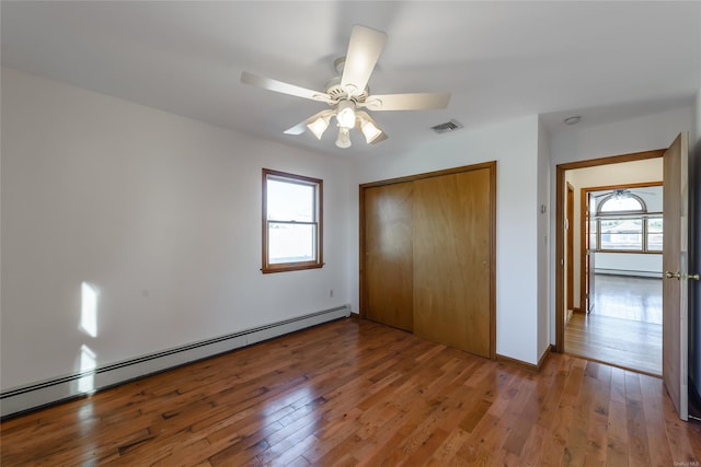 unfurnished bedroom featuring hardwood / wood-style floors, a closet, a baseboard heating unit, and ceiling fan