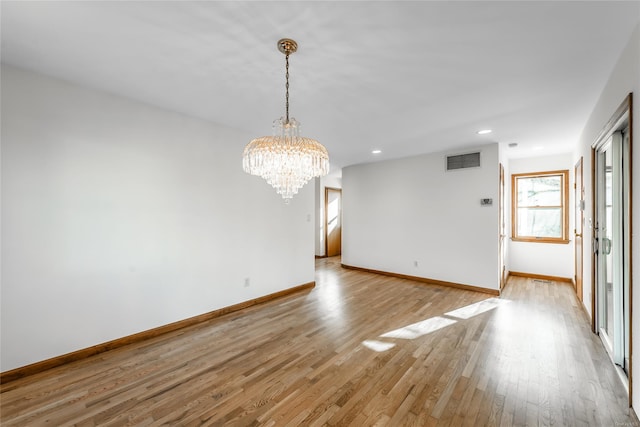 empty room with a notable chandelier and light hardwood / wood-style flooring