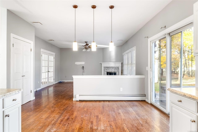 unfurnished living room with hardwood / wood-style floors, ceiling fan, a stone fireplace, and baseboard heating