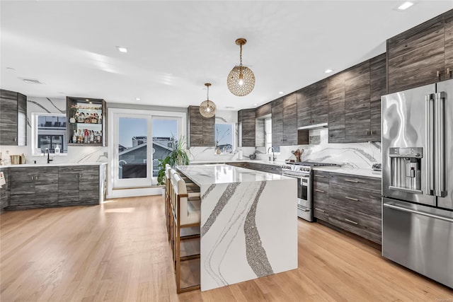 kitchen with sink, hanging light fixtures, appliances with stainless steel finishes, a kitchen island, and light wood-type flooring