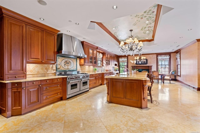 kitchen with pendant lighting, a center island, double oven range, a raised ceiling, and wall chimney range hood