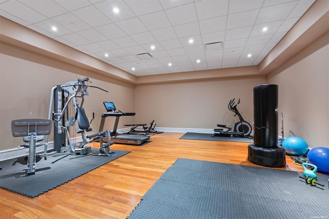 exercise room with a paneled ceiling and hardwood / wood-style flooring