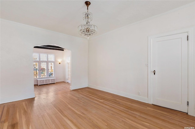 spare room featuring a notable chandelier, light wood-type flooring, and crown molding