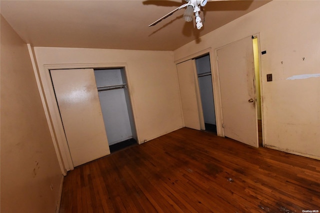 unfurnished bedroom featuring two closets, dark hardwood / wood-style floors, and ceiling fan