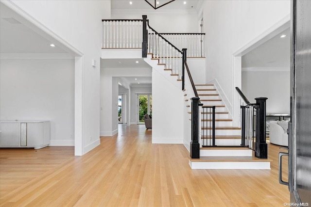 foyer entrance with crown molding, light hardwood / wood-style flooring, and a towering ceiling