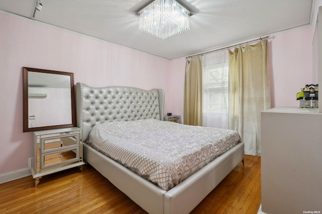 bedroom featuring an AC wall unit, a chandelier, and hardwood / wood-style flooring