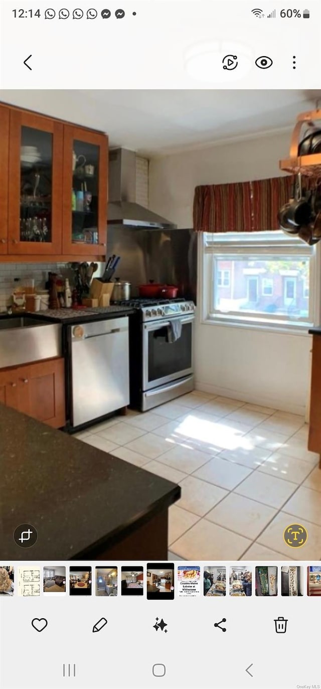 kitchen featuring light tile patterned floors, wall chimney range hood, backsplash, and appliances with stainless steel finishes