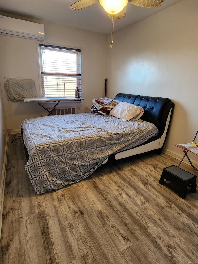 bedroom with ceiling fan, a wall mounted AC, and hardwood / wood-style floors