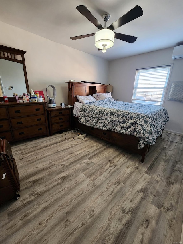 bedroom with a wall mounted air conditioner, light hardwood / wood-style flooring, and ceiling fan