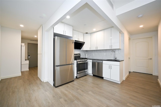 kitchen with appliances with stainless steel finishes, sink, exhaust hood, white cabinets, and light hardwood / wood-style floors