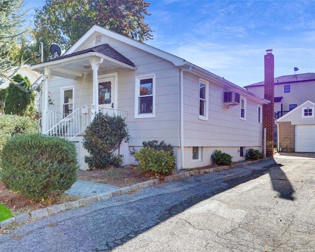 bungalow-style home with a wall mounted air conditioner, a garage, and an outbuilding