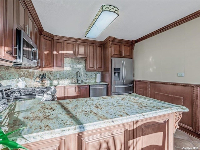 kitchen featuring light stone countertops, appliances with stainless steel finishes, kitchen peninsula, ornamental molding, and sink