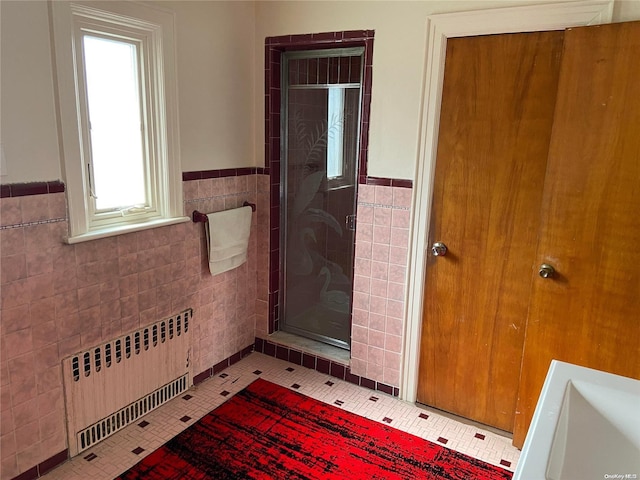 bathroom with tile patterned flooring, walk in shower, radiator, and tile walls