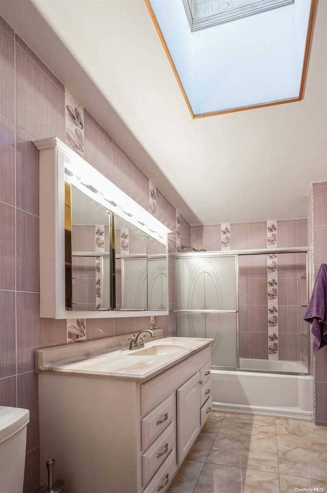 full bathroom featuring vanity, combined bath / shower with glass door, a skylight, toilet, and tile walls