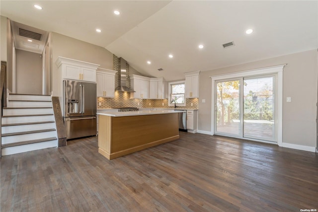 kitchen featuring wall chimney range hood, vaulted ceiling, a kitchen island, white cabinetry, and stainless steel appliances