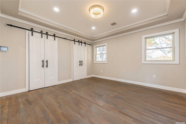 unfurnished bedroom featuring a tray ceiling, a barn door, dark hardwood / wood-style floors, and multiple windows