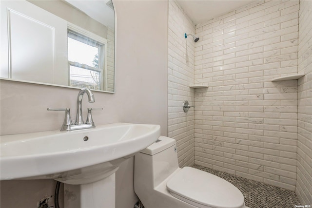 bathroom featuring tiled shower, sink, and toilet