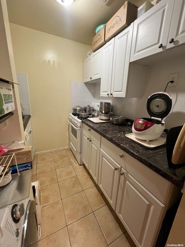 kitchen featuring decorative backsplash, dark stone counters, white range with gas cooktop, light tile patterned floors, and white cabinetry