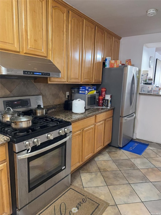 kitchen with backsplash, light tile patterned floors, dark stone counters, and appliances with stainless steel finishes