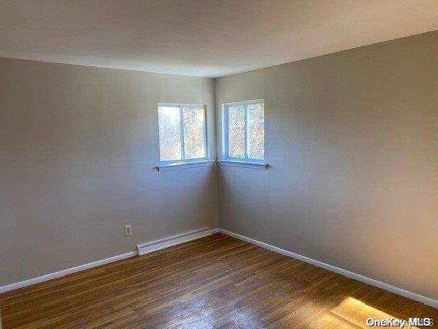 empty room featuring baseboard heating and dark wood-type flooring