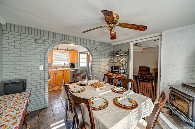 tiled dining area featuring brick wall, ceiling fan, crown molding, and sink