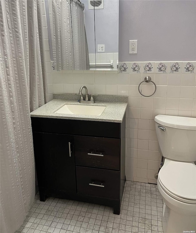 bathroom featuring tile patterned floors, vanity, tile walls, and toilet