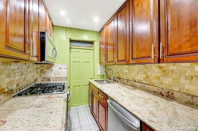 kitchen featuring sink, decorative backsplash, light stone countertops, appliances with stainless steel finishes, and light tile patterned flooring