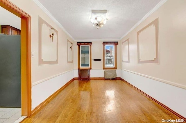 spare room with crown molding, radiator heating unit, a notable chandelier, and light wood-type flooring