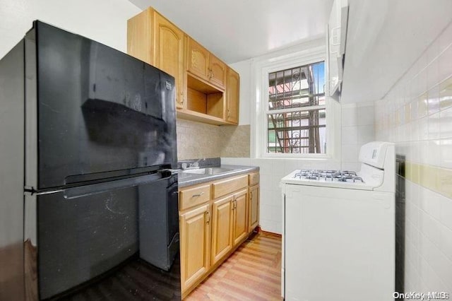 kitchen featuring white range oven, black fridge, tile walls, and light brown cabinetry