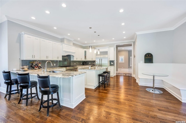 kitchen with a center island with sink, sink, hanging light fixtures, dark wood-type flooring, and white cabinets