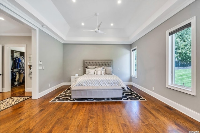 bedroom featuring ceiling fan, hardwood / wood-style floors, a walk in closet, and a raised ceiling