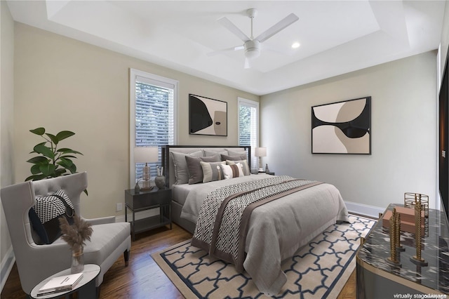 bedroom with ceiling fan, dark wood-type flooring, and a tray ceiling