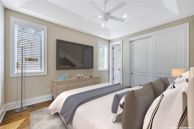 bedroom with ceiling fan, dark hardwood / wood-style floors, and a tray ceiling