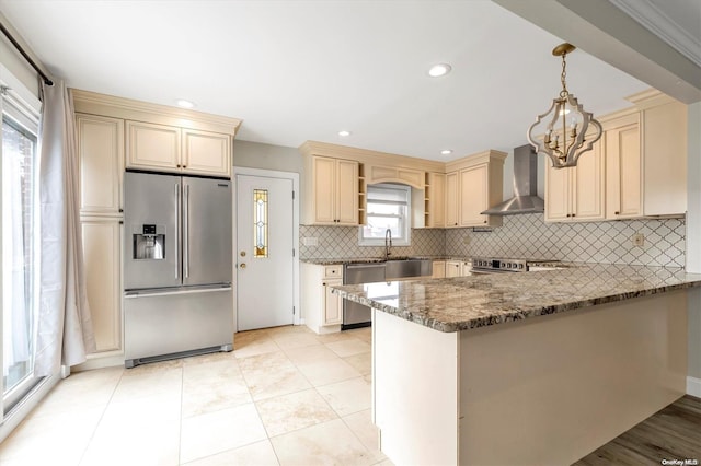 kitchen featuring wall chimney exhaust hood, dark stone countertops, kitchen peninsula, pendant lighting, and appliances with stainless steel finishes