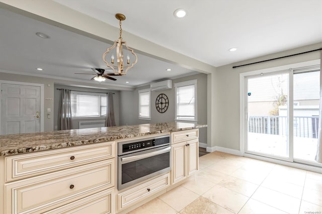 kitchen featuring cream cabinets, oven, ceiling fan with notable chandelier, hanging light fixtures, and light stone counters