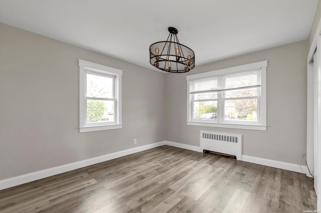 unfurnished dining area with light hardwood / wood-style floors, radiator, and an inviting chandelier